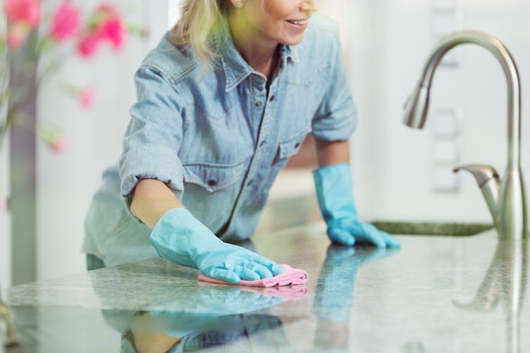 A woman cleaning the kitchen counter with a pink cloth.