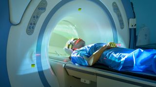 A patient wearing a hospital gown enters a Magnetic Resonance Imaging (MRI) machine.