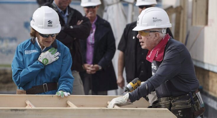 Former President Jimmy Carter and Rosalynn Carter wearing white hard hats at a construction site