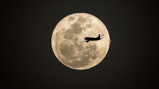 a beautiful moon with the shadow of an airplane flying in the foreground