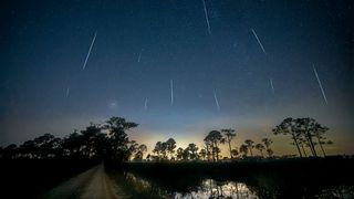 A long shot of a meteor shower over a lake and trees