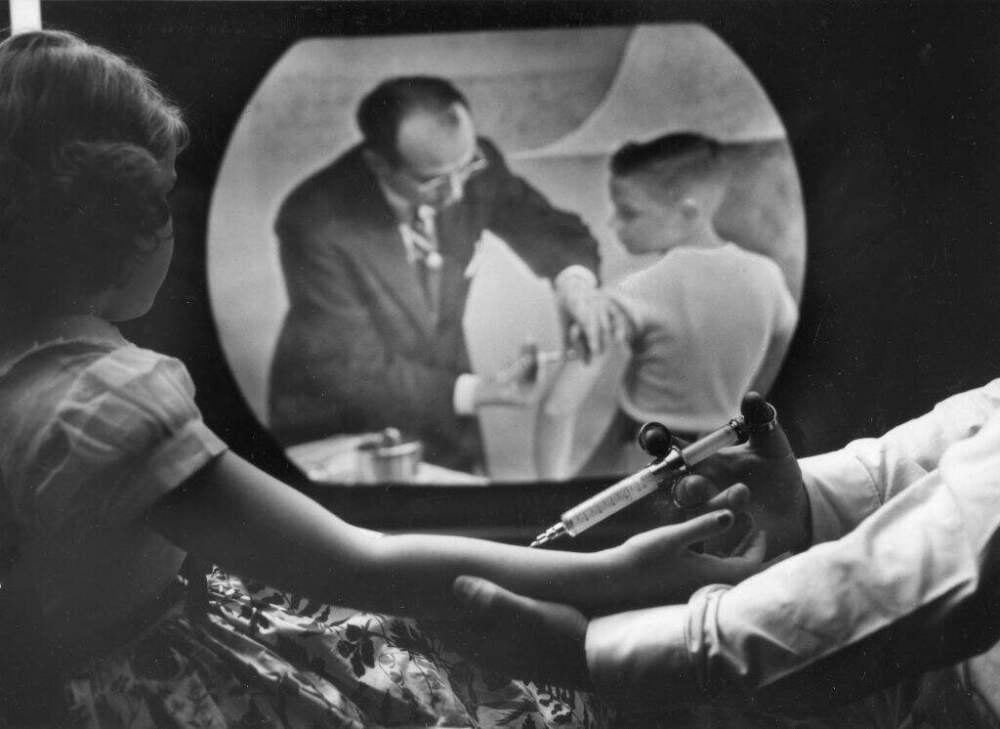 When an 8-year-old girl receives a polio vaccine, she watches a closed-circuit television broadcast (showing Dr. Jonas Salk vaccinating a boy) of a training program for doctors and scientists, in New York, New York, April 12. 1955. (PhotoQuest/Getty Images)