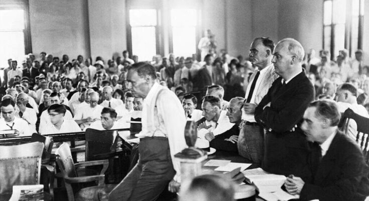 Defense attorney Clarence Darrow leans on a table during Scopes "A monkey" A case in which biology teacher John T. Scopes was prosecuted for teaching evolution to his class. Scopes sits at Darrow's right hand with folded arms. (Getty Images)